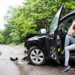 Young woman in the damaged car after a car accident, making a phone call.