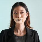 Asian woman is silenced with adhesive tape across her mouth