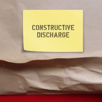 Torn office envelope with stick note written Constructive Discharge (Constructive Dismissal) where employee is forced to leave or quit because employer’s conduct hostile workplace or intolerable situation