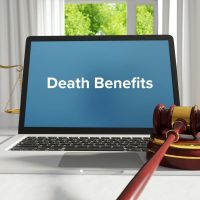 Death Benefits – Law, Judgment, Web. Laptop in the office with term on the screen. Hammer, Libra, Lawyer.