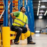 A warehouse worker having back pain and rubbing it.
